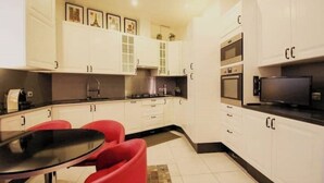 Een moderne keuken met witte kasten, een zwart aanrecht en rode stoelen rond een glazen tafel.