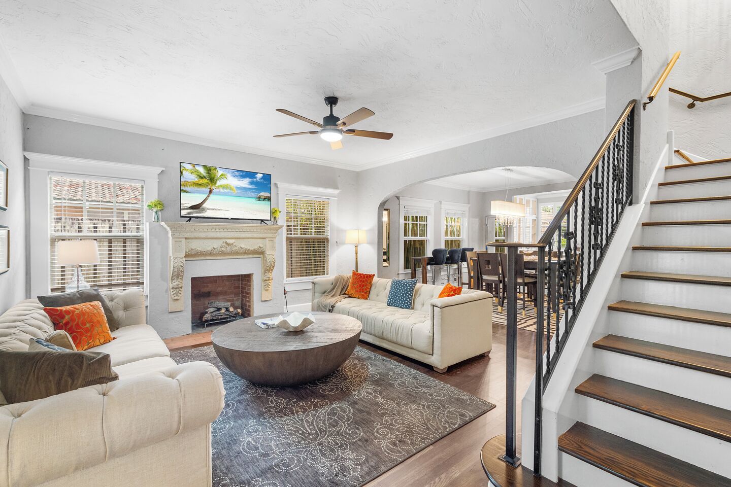 A spacious living room with a fireplace, a ceiling fan, and a staircase.