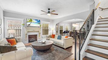 A spacious living room with a fireplace, a ceiling fan, and a staircase.