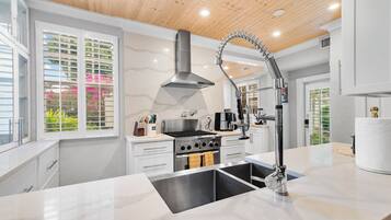 A modern kitchen with a central island, stainless steel appliances, and a high ceiling with wooden beams.