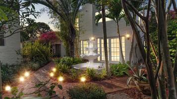 A garden with a white fountain, surrounded by various plants and a brick pathway.