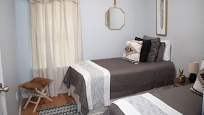 A bedroom with a bed, a small stool, a nightstand, a lamp, a mirror, and a window with curtains. - Boot Scoot'n In the Stockyards. 3 bedrooms/2 bath (Fort Worth)