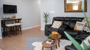 A living room with a black leather sofa, a small wooden coffee table, a patterned rug, and a television mounted on the wall. - Boot Scoot'n In the Stockyards. 3 bedrooms/2 bath (Fort Worth)