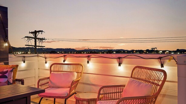 An outdoor seating area with wicker chairs and a table, overlooking a cityscape at dusk. - Lookout Getaway: Luxury 4 Bedroom, Rooftop Deck (Chattanooga)