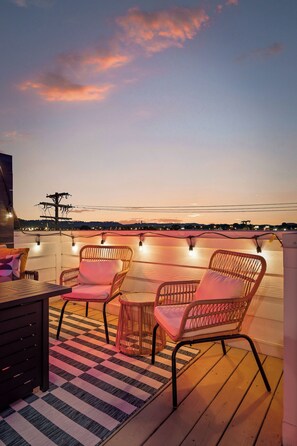 Un espace extérieur aménagé avec des chaises et une table en osier, offrant une vue sur le paysage urbain au crépuscule.