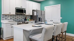 A kitchen with white cabinets, a microwave, a refrigerator, a sink, and a dining area with chairs. - Lookout Getaway: Luxury 4 Bedroom, Rooftop Deck (Chattanooga)