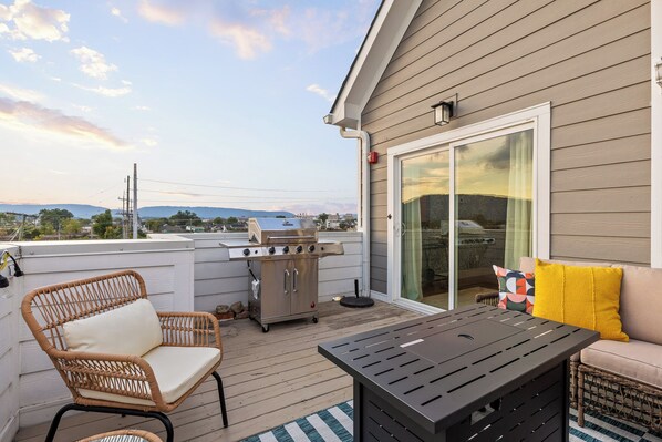 Une terrasse extérieure couverte, équipée d’un barbecue, de chaises en osier, d’une table et d’un canapé avec des coussins.