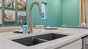 A kitchen with a stainless steel sink, a window, and framed pictures on the wall. - Lookout Getaway: Luxury 4 Bedroom, Rooftop Deck (Chattanooga)