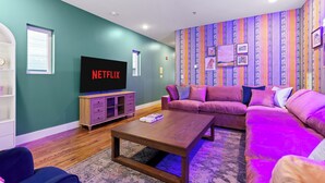 A living room with a sectional sofa, a coffee table, a TV, and a wall with vertical stripes. - Lookout Getaway: Luxury 4 Bedroom, Rooftop Deck (Chattanooga)