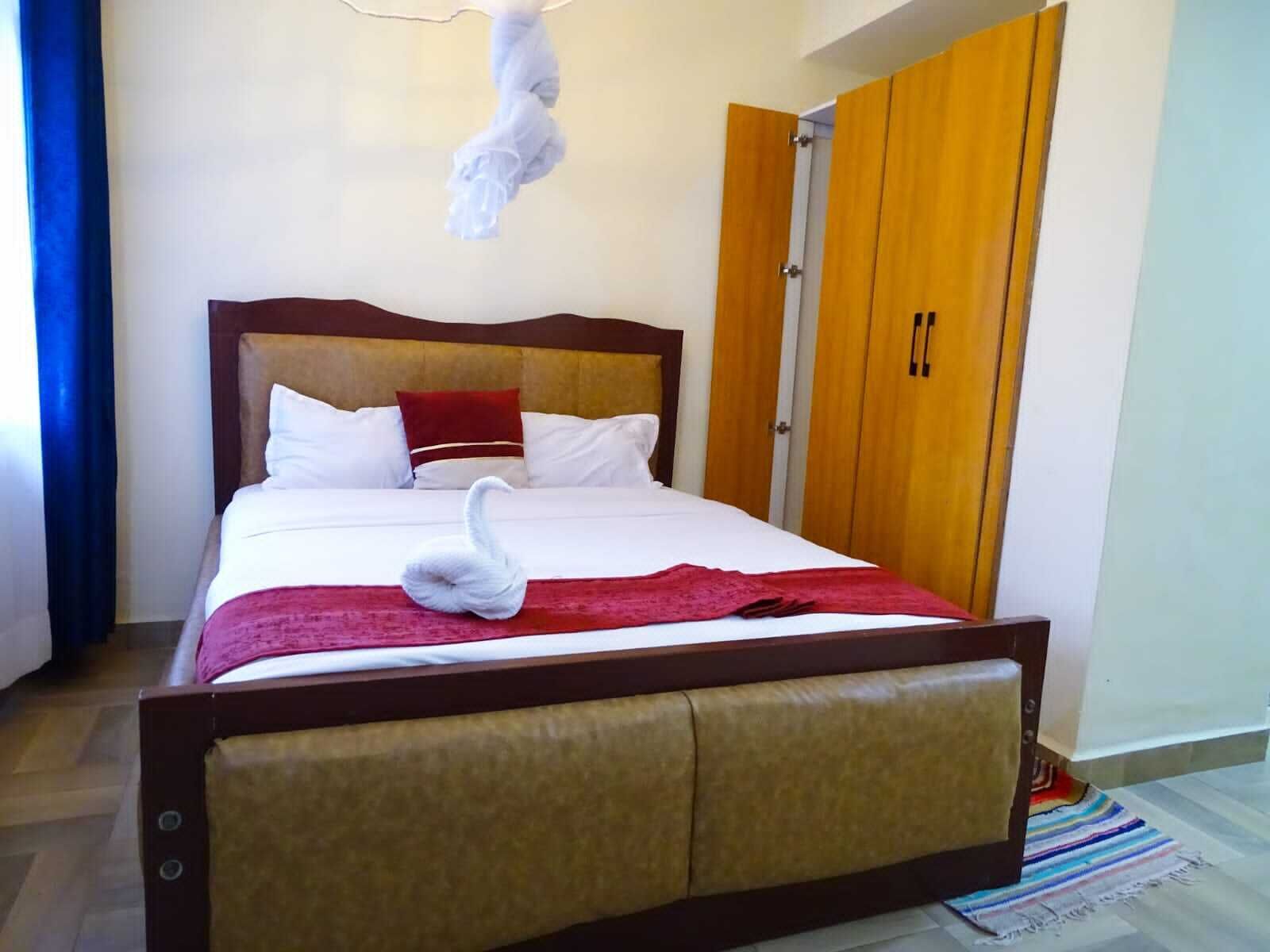 A hotel room with a bed, wooden wardrobe, and a swan-shaped decoration on the bed.