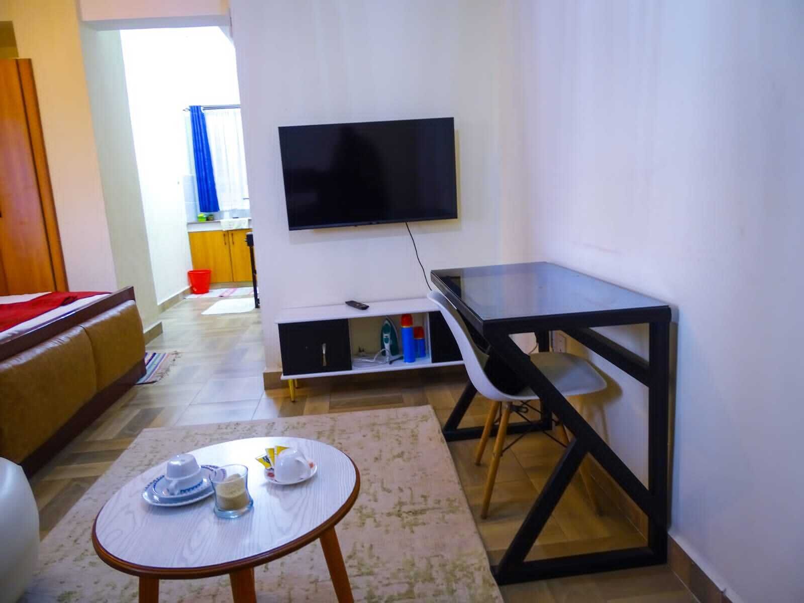 A living room with a sofa, a coffee table, a TV mounted on the wall, and a small table with a chair.