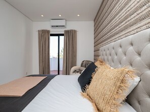 A bedroom with a large bed, a tufted headboard, and a view through a window with curtains.