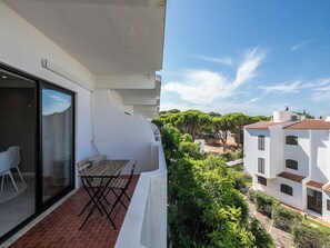 A balcony with a table and chairs, overlooking a residential area with trees and buildings.