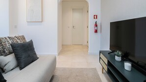 A modern living room with a sofa, a flat-screen TV, a console table, and a hallway leading to a door. - Palm Beige Apartment, Vilamoura, Algarve (Quarteira)