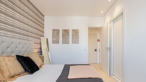 A modern hotel room with a large bed, a decorative wall, and a door leading to another room. - Palm Beige Apartment, Vilamoura, Algarve (Quarteira)