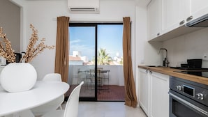 A modern kitchen with a dining area, a sliding glass door to a balcony, and a view of the cityscape. - Palm Beige Apartment, Vilamoura, Algarve (Quarteira)