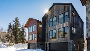 Un bâtiment moderne à plusieurs étages, doté de grandes fenêtres et d’un garage, entouré de neige et d’arbres.