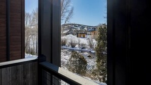 Une vue par une fenêtre à cadre en bois, donnant sur un paysage enneigé avec des bâtiments et des arbres.