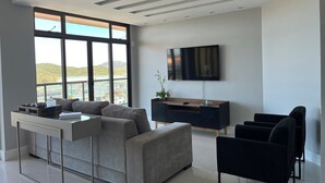 Een moderne woonkamer met een bank, een aan de muur bevestigde televisie en een groot raam met uitzicht op een glooiend landschap.