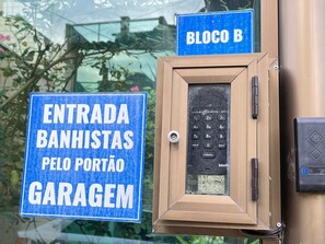 Ein blaues Schild mit weißer Schrift, das "ENTRADA BANHISTAS PELO PORTÃO GARAGEM" zeigt, und eine Tastatureinsatzschleuse mit der Aufschrift "BLOCO B".