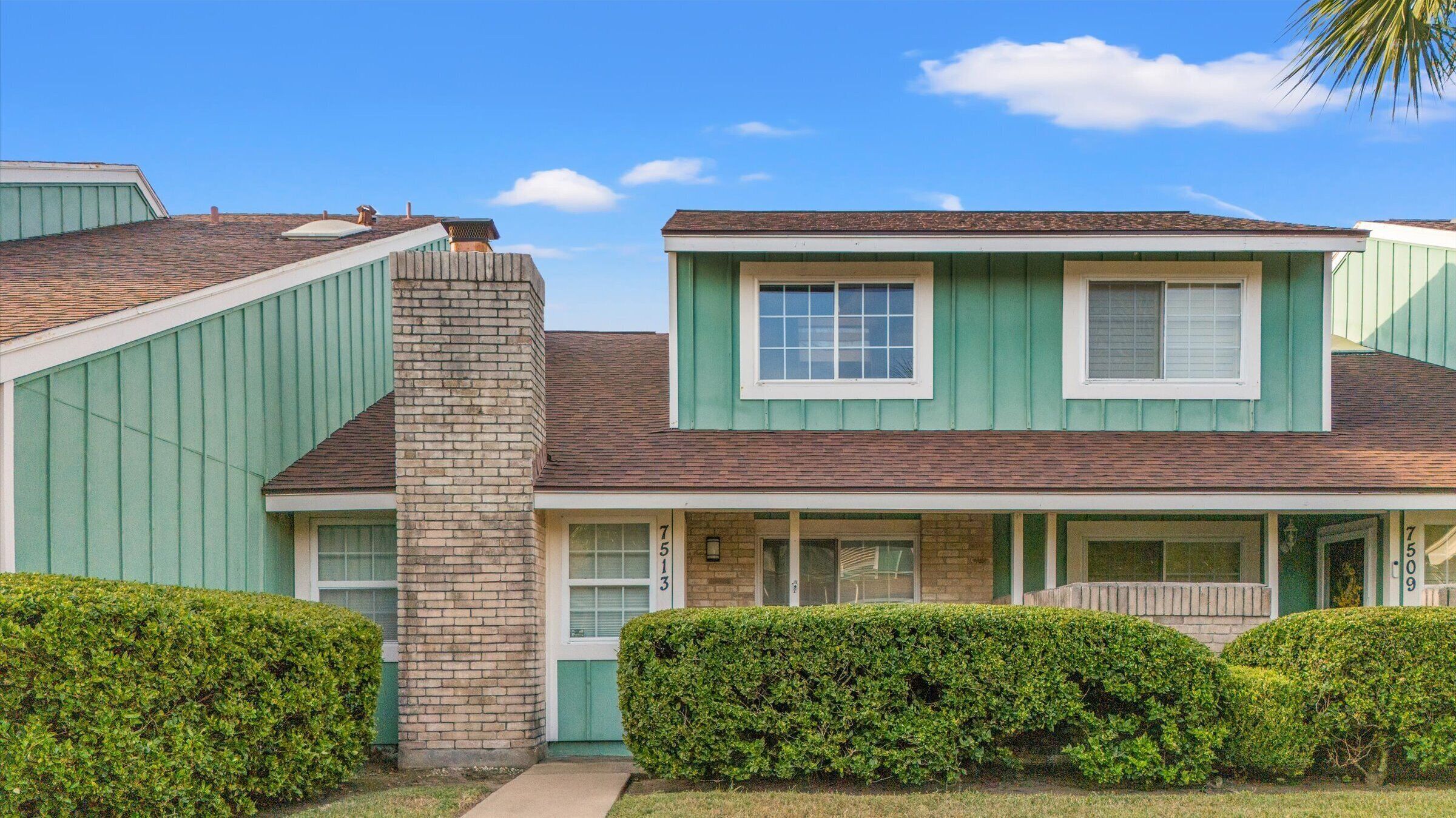 A two-story house with a green exterior, a brick chimney, and a front porch.