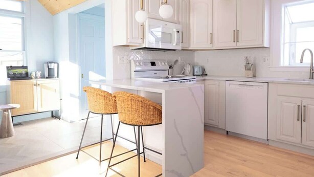 Una cocina moderna con armarios blancos, una isla central con taburetes de bar, microondas y lavavajillas.