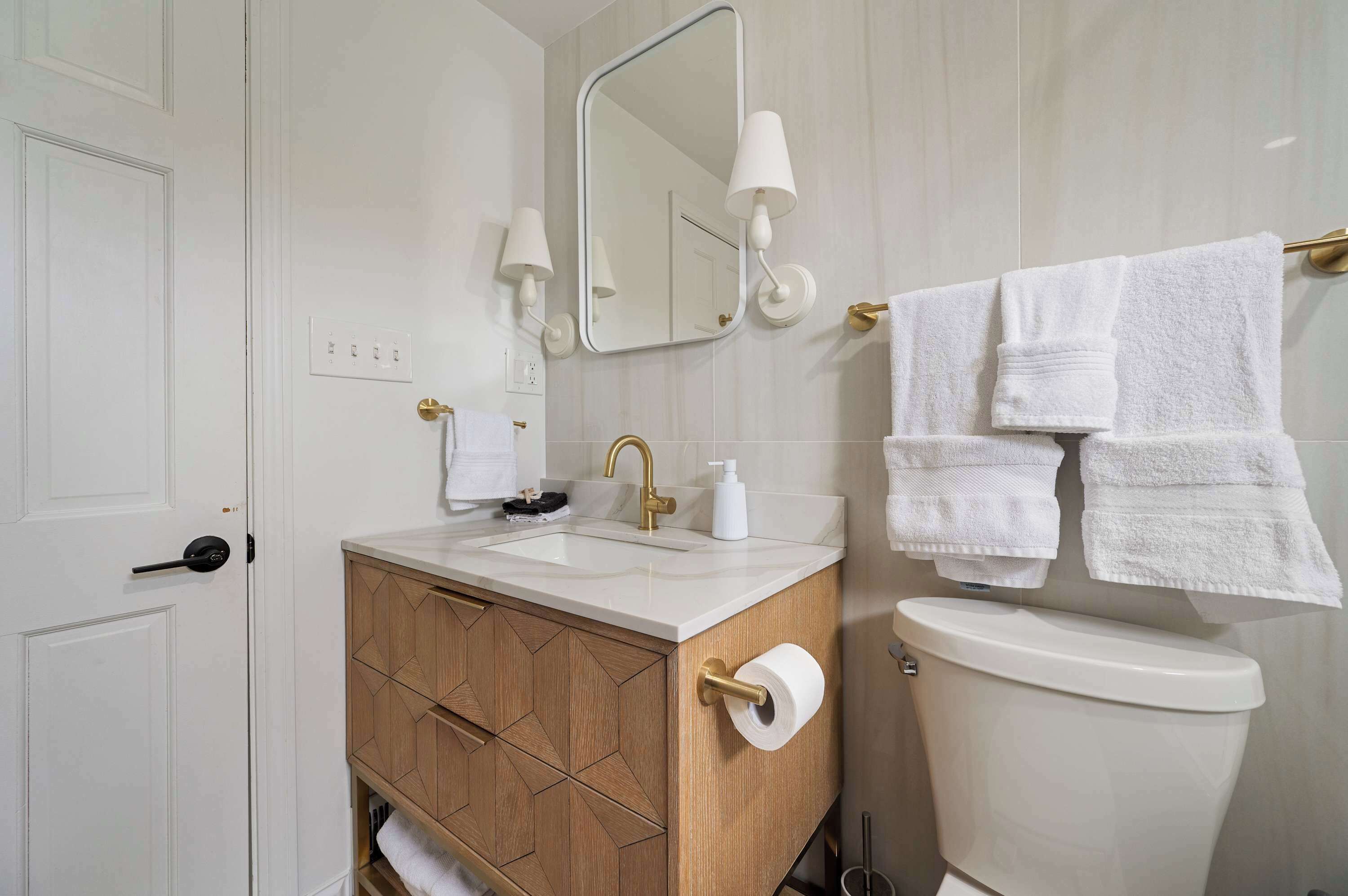 Et badeværelse med hvid vask, trækommode, toilet, spejl og håndklæder.