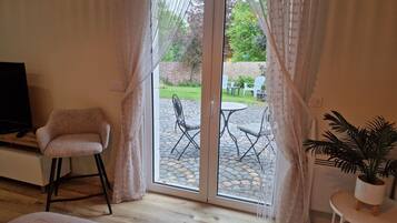 Ein Zimmer mit Fernseher, einem gepolsterten Sessel, einem kleinen Tisch mit Pflanze und einer Schiebeglastür zu einer Außenpatio mit Stühlen und Tisch.
