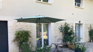 Ein Innenhof mit Tisch und Stühlen unter einem großen Sonnenschirm, umgeben von Blumentöpfen und einer Steinmauer.