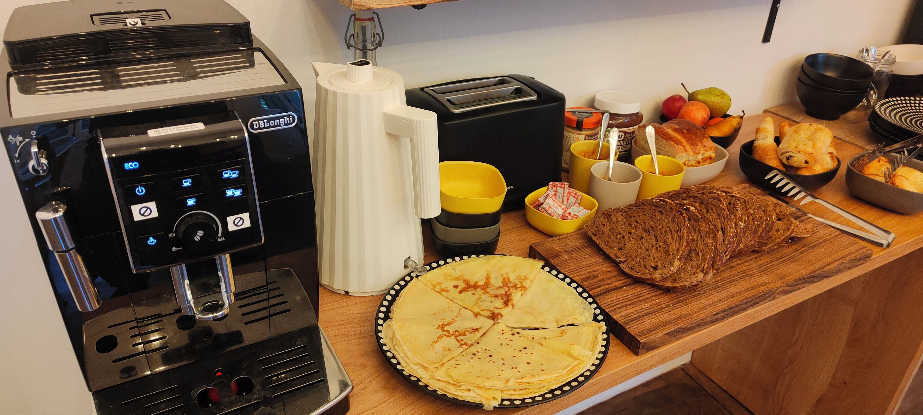 Una cuina amb una màquina de cafè, torradora i diferents aliments sobre el taulell.