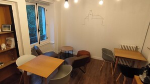 Quarto com uma mesa de madeira, cadeiras, uma estante e uma parede com um desenho simples.