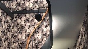 Escadaria em espiral com papel de parede floral, corrimão de madeira e uma cadeira amarela em primeiro plano.