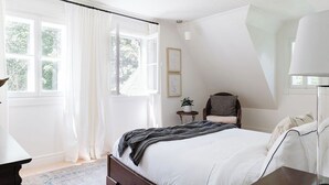 A bedroom with a large bed, a chair, a small table with a plant, and a lamp. - Le Pavillon | Comfort in Nature (Saint-Côme)