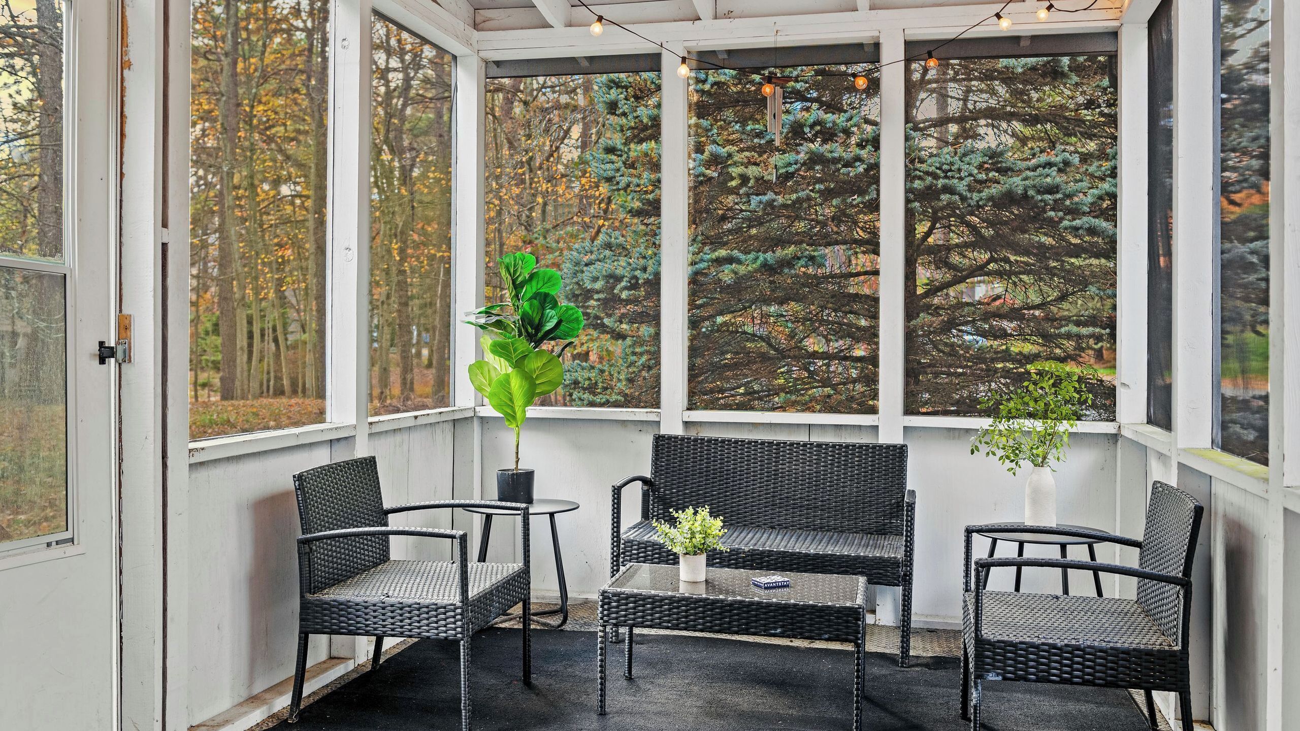 A covered porch with wicker furniture, a potted plant, and a view of trees.