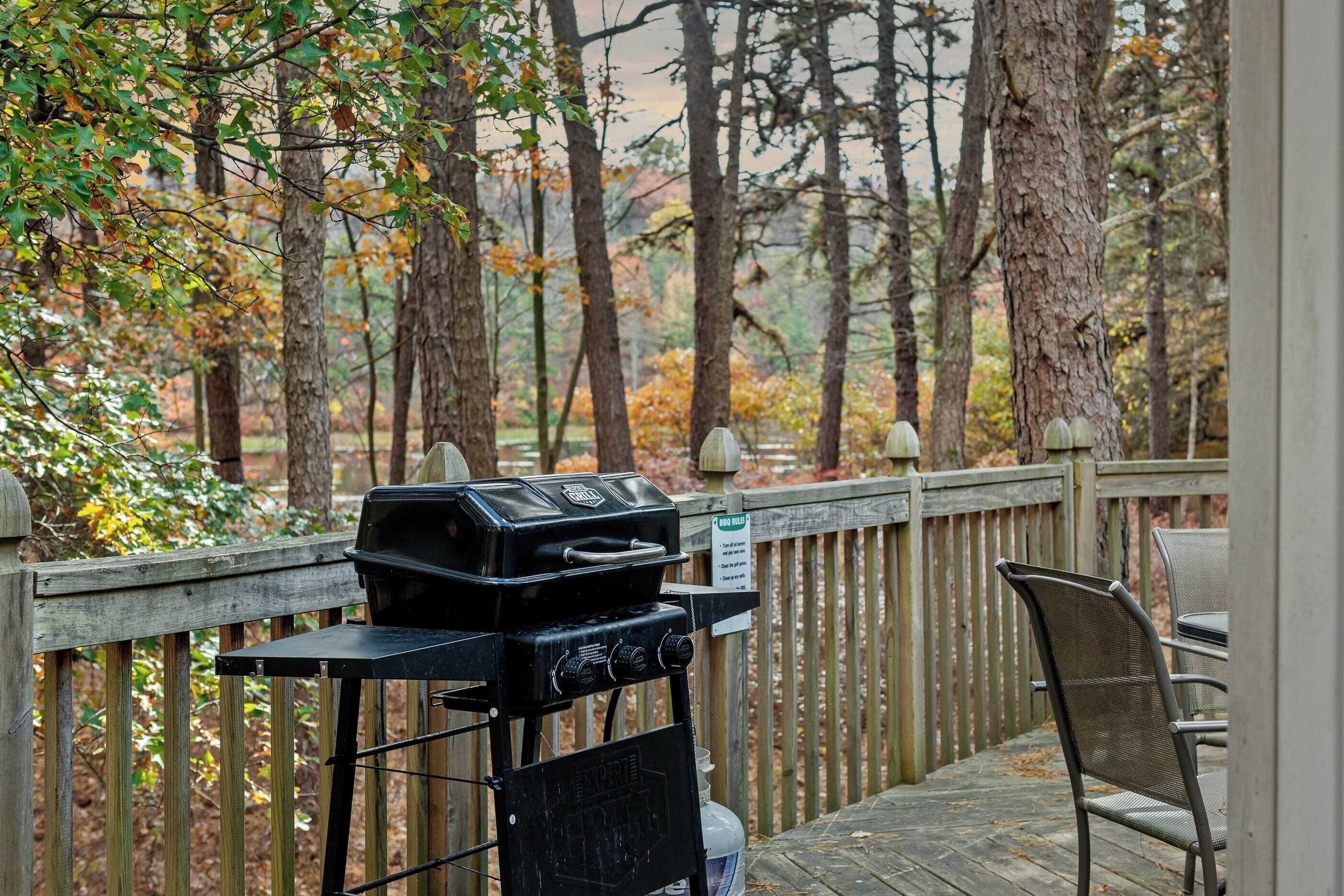 A barbecue grill on a wooden deck with a view of trees.