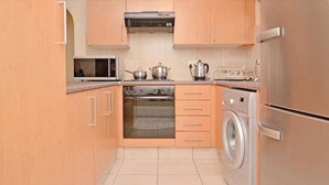 A compact kitchen with wooden cabinets, a stainless steel refrigerator, a microwave, an oven, and a washing machine.