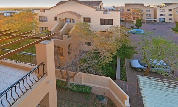 A residential building with multiple balconies, a parking area, and a small garden.