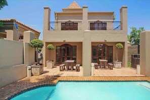 Une maison à deux étages avec une piscine, du mobilier d’extérieur et un balcon.