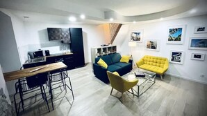 Un espace de vie compact comprenant un coin cuisine, un canapé, un fauteuil jaune et une table basse.