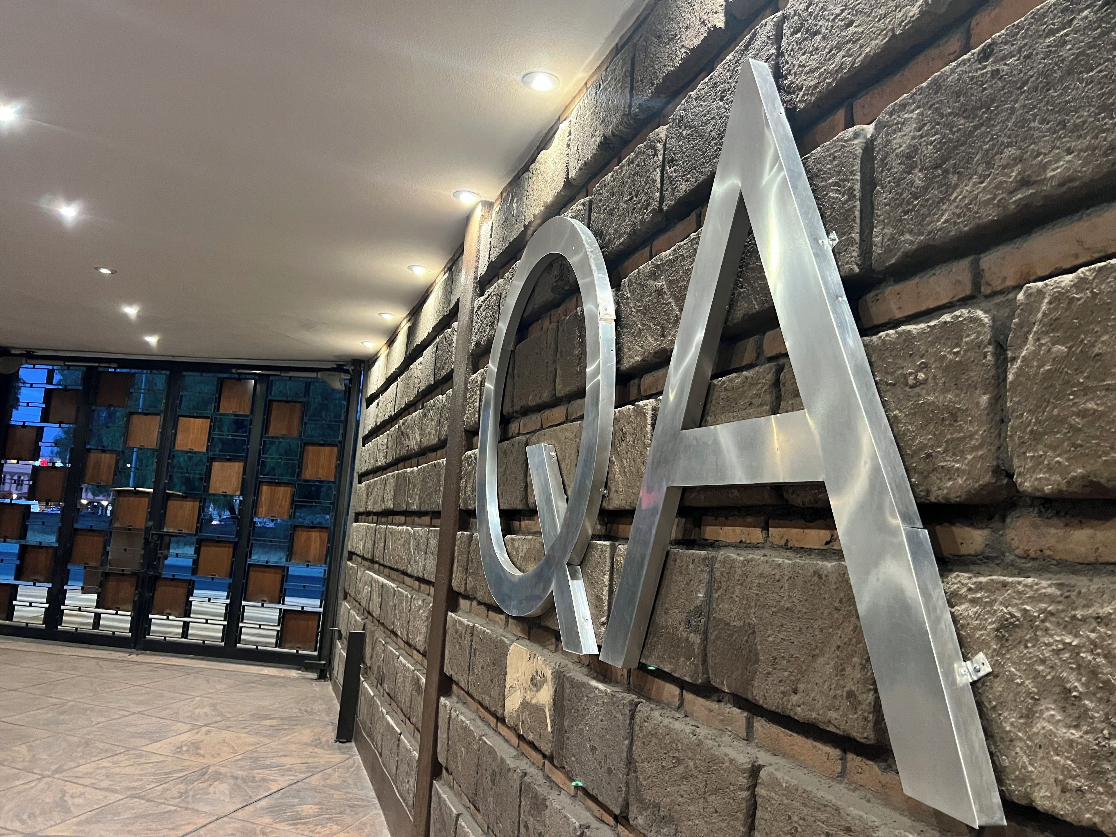 Eine Wand mit großen, metallischen Buchstaben, die „Q&A“ bilden, ist an einer Steinsäule angebracht.