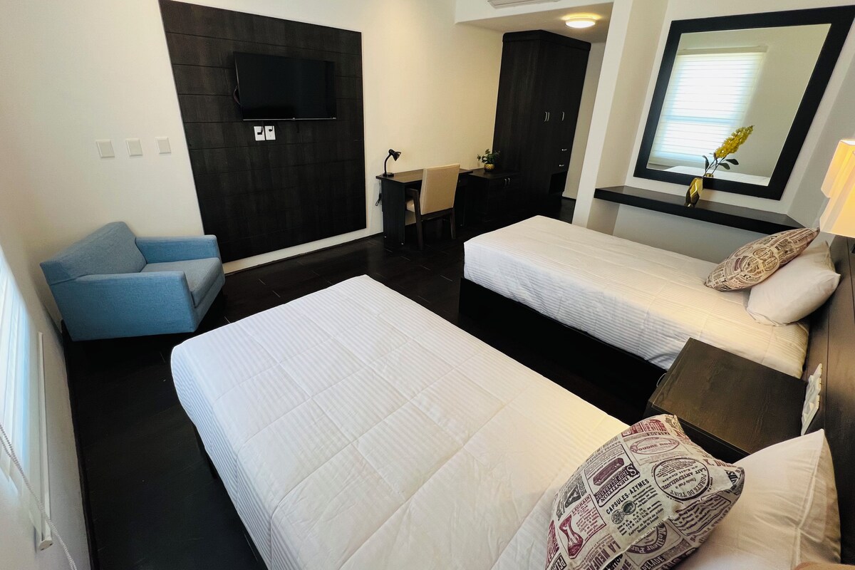 Une chambre d’hôtel avec deux lits, un bureau, une chaise, une télévision et un miroir.