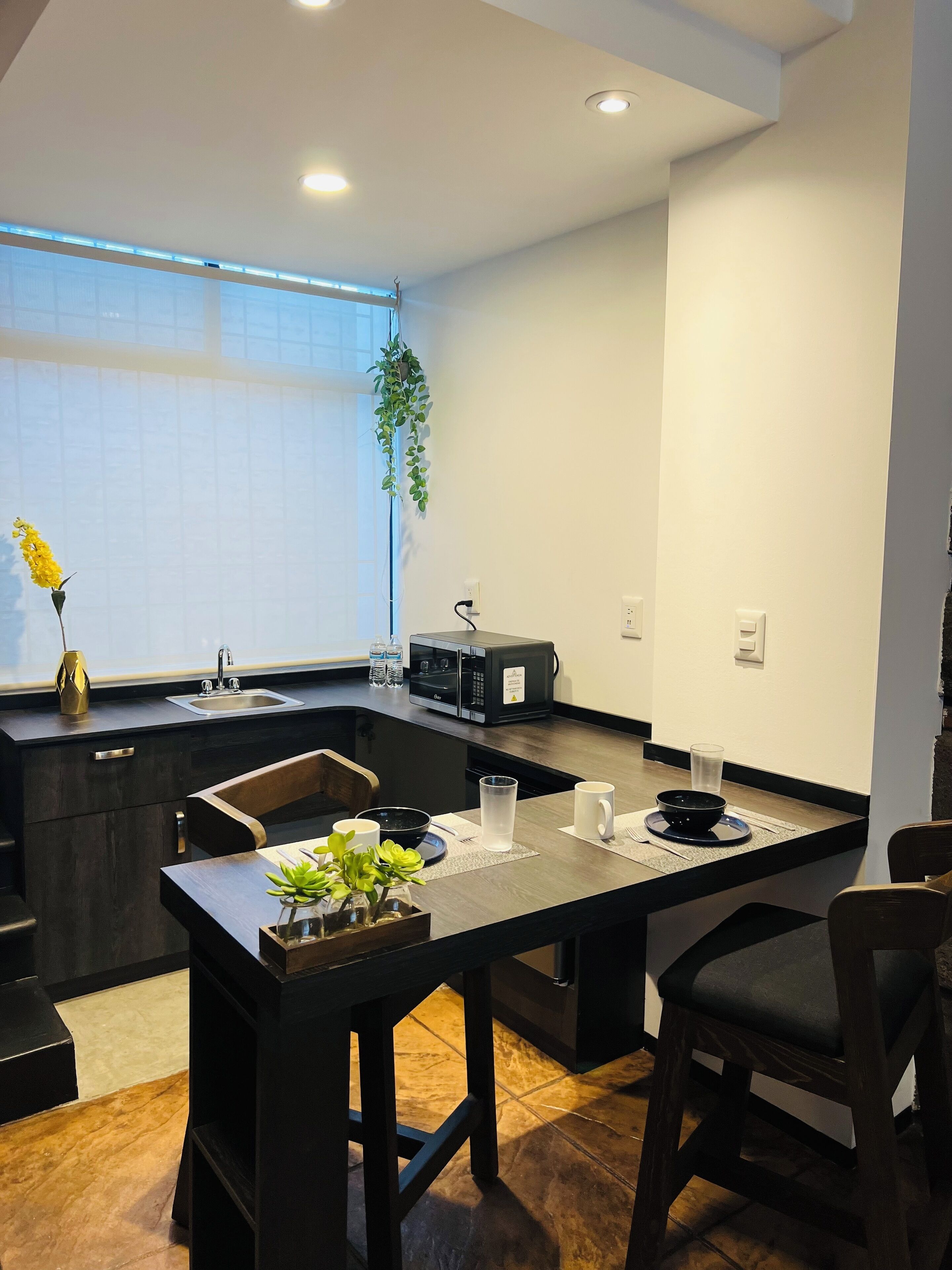 Una cocina moderna con microondas integrado, un lavamanos y una zona de comedor con mesa y sillas.