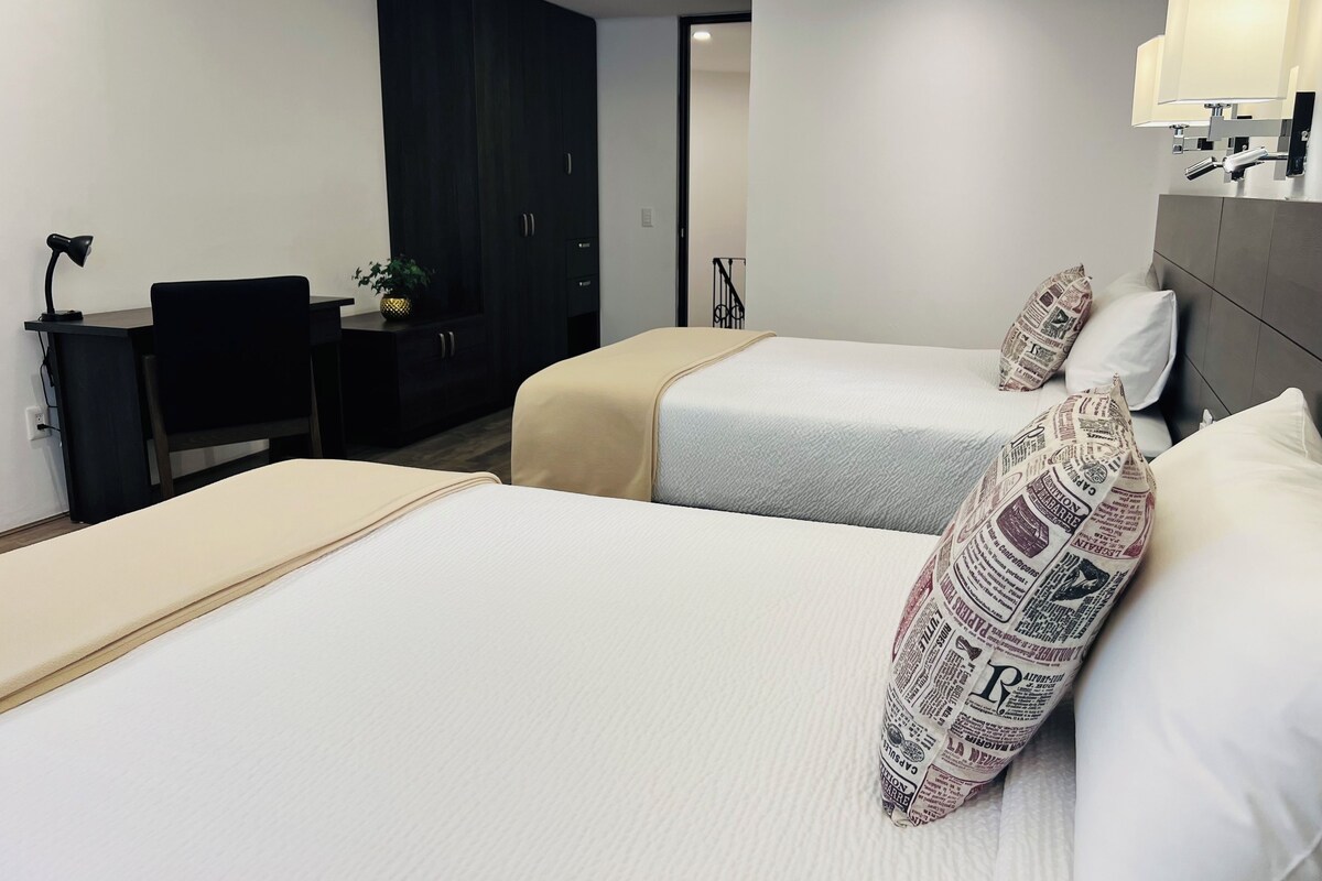 Une chambre d’hôtel avec deux lits, un bureau, une chaise, une armoire et une lampe.