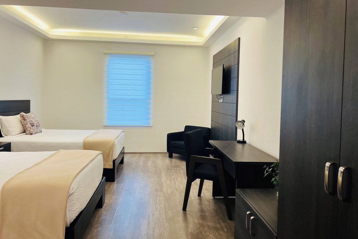 Een moderne hotelkamer met twee bedden, een bureau, een stoel, een televisie en een raam met jaloezieën.
