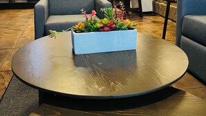 Un salon moderne avec une table basse ronde, des canapés gris, un lampadaire noir et un mur en briques.