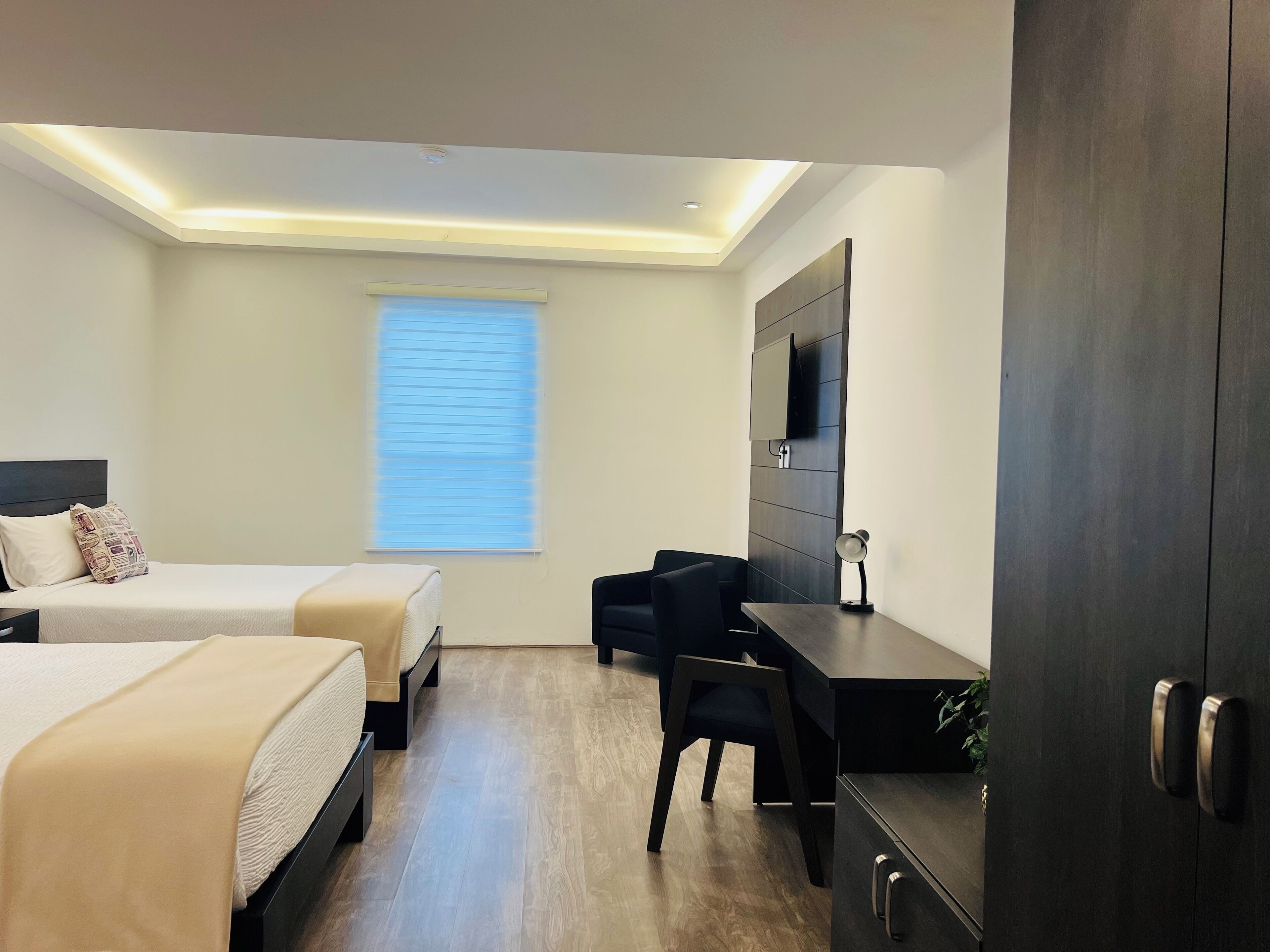Una habitación de hotel moderna con dos camas, un escritorio, una silla, un televisor y una ventana con persianas.