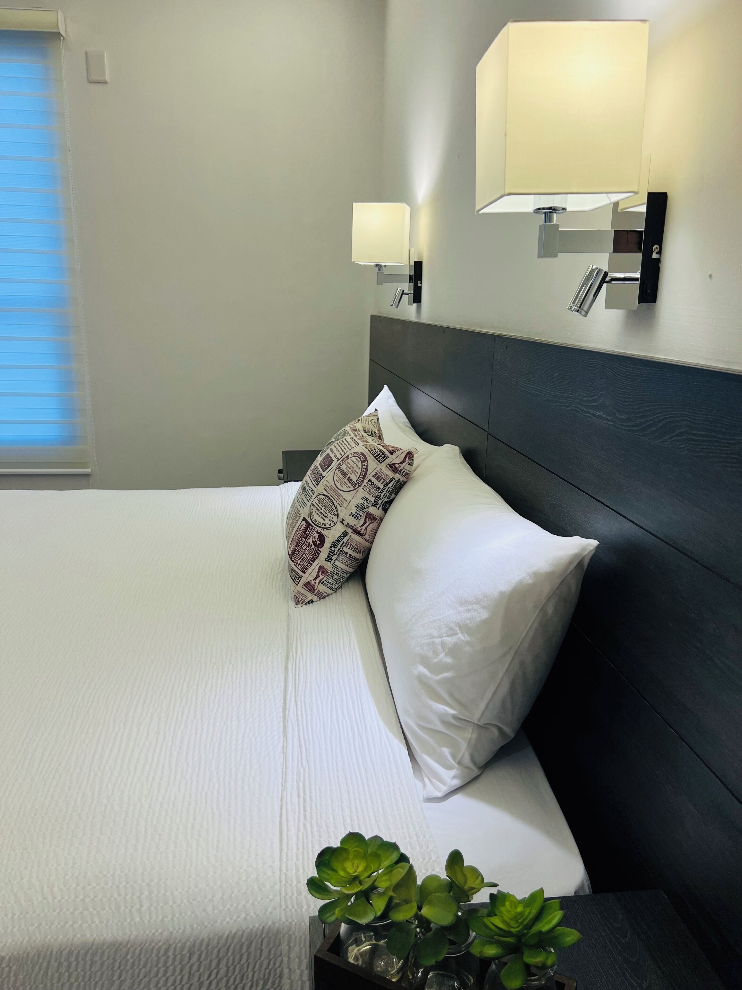 A neatly made bed with white linens and patterned pillows, a dark headboard, and bedside lamps.