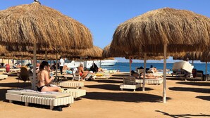 En strand med parasoller av halm, solstolar och människor som kopplar av.