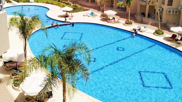 Ett hotell med en stor pool, flera balkonger och utsikt över stranden.