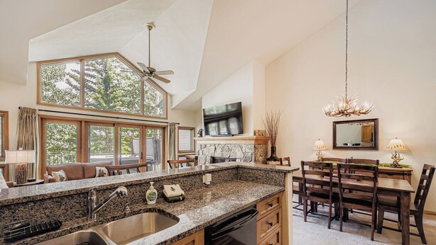 A spacious kitchen with granite countertops, a built-in oven, and a dining area with wooden chairs and a chandelier.